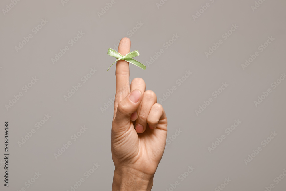 Woman showing index finger with tied bow as reminder on grey background, closeup Woman showing index finger with tied bow as reminder on grey background, closeup