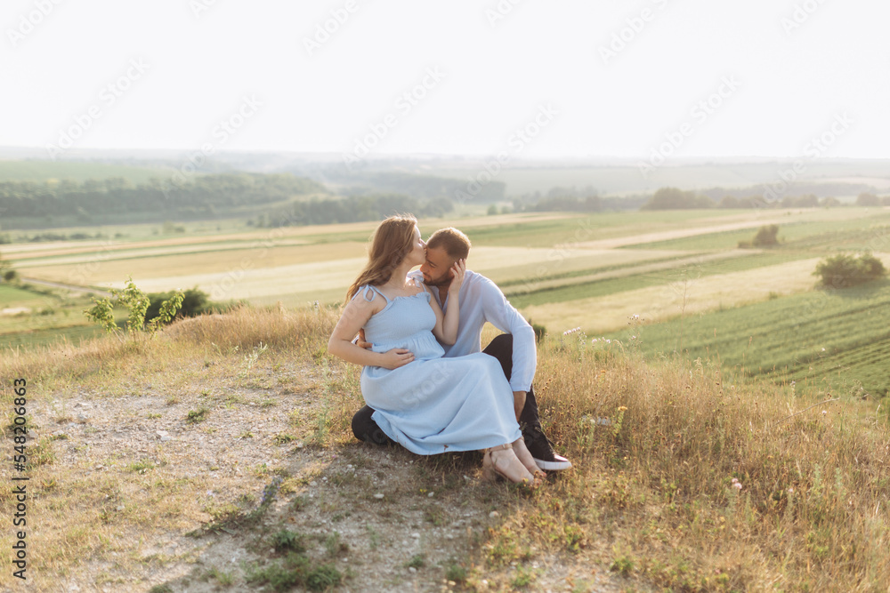 Portrait of a lovely couple standing together on the greenfield. Happy couple expecting a baby, young family concept