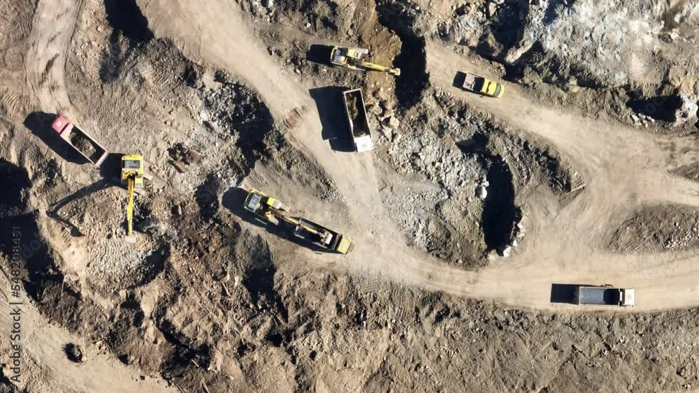 Industrial mine excavators are digging the soil in the construction site and loading trucks. Aerial drone top view. Industrial mine excavators are digging the soil in the construction site and loading trucks. Aerial drone top view.