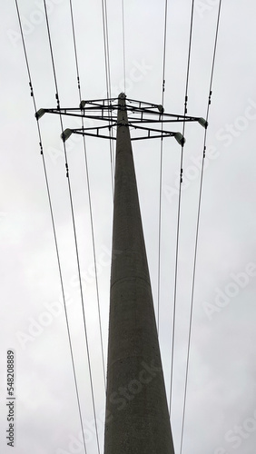 A tall concrete pole with electrical wires. A cement pylon of a power line under a light gray sky that is covered with clouds. Oprah is holding several high voltage metal wires. photo