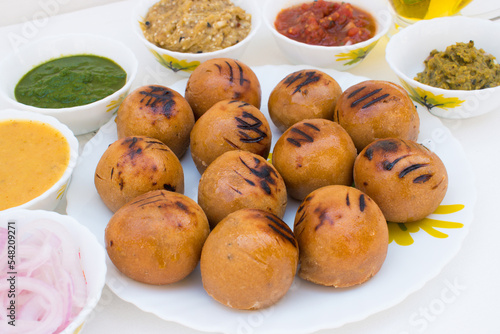 Litti in white plate with tomato, brinjal, potato, pointed gaurd and coriander chutney or chokha and ghee. It is popular in Bihar, Uttar Pradesh and Jharkhand. White background photo