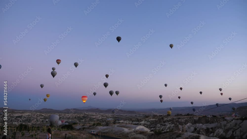 Many balloons hovering in the pre-dawn sky above the mountain landscape. Colorful balloons flying over the valleys. The famous city of Cappadocia, Turkey