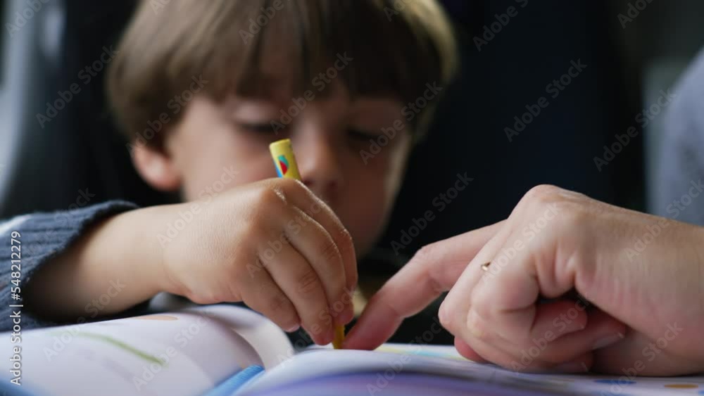 Child doing homework closeup face. Mother hand pointing at drawing figure on paper. Parent helping little boy with homeschooling Child doing homework closeup face. Mother hand pointing at drawing figure on paper. Parent helping little boy with homeschooling