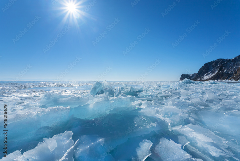Winter landscape of frozen Baikal Lake on a frosty sunny February day. View of ice hummocks and blue pieces of ice near the rocky shore of Olkhon Island. Winter travel and outdoor recreation