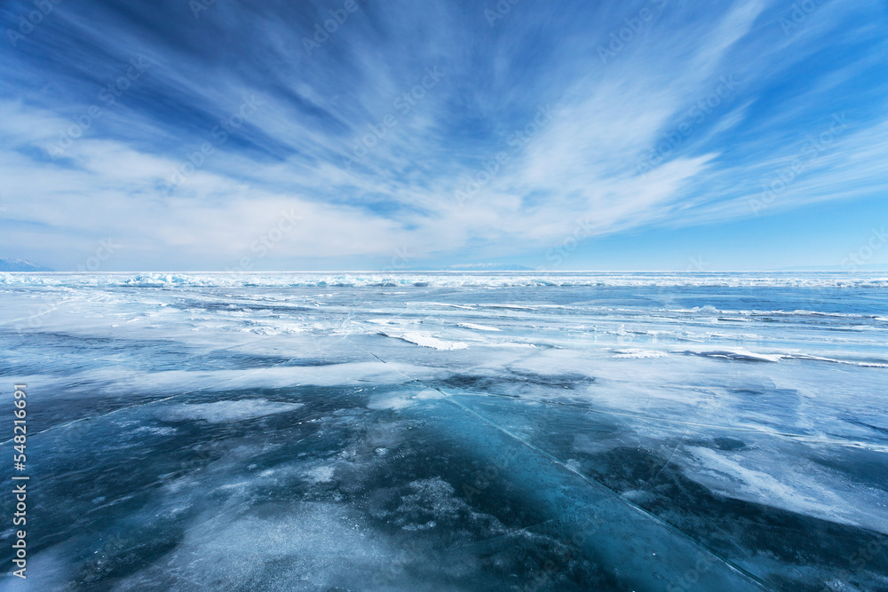 Unusual winter landscape of frozen Baikal Lake on February day. Above icy endless desert, beautiful stratus clouds adorn the blue sky. Natural cold background. Winter travel and outdoor recreation