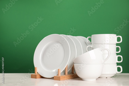 Set of clean dishware on white table against green background