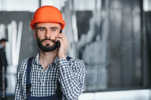 Portrait of Professional Heavy Industry Engineer Worker Wearing Safety Uniform, Hard Hat Smiling. In the Background Unfocused Large Industrial Factory.