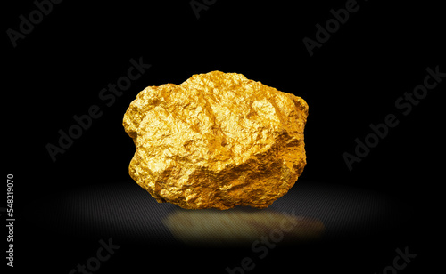Gold nugget on a black background. Precious metal, wealth concept, investment, contribution. Stone is lit from above with reflection against a textured glossy background.