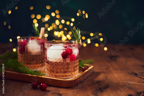 Alcoholic cocktail or non-alcoholic cocktail with vodka and cranberries with ice with fir branches and glowing garland for christmas on wooden background