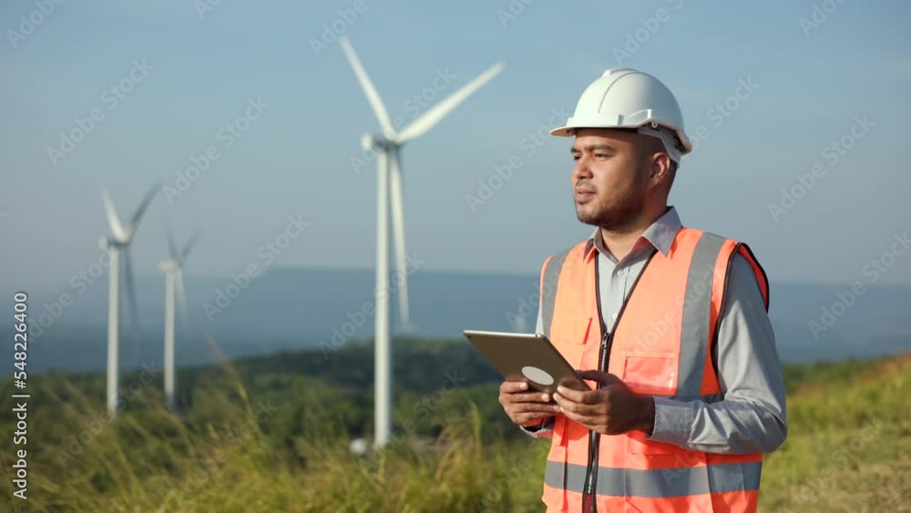 Confident engineer using tablet control wind turbines windmill energy farm. Engineering Sustainable technology wind power turbine for generation electricity. Renewable energy, Green energy concept. Confident engineer using tablet control wind turbines windmill energy farm. Engineering Sustainable technology wind power turbine for generation electricity. Renewable energy, Green energy concept.