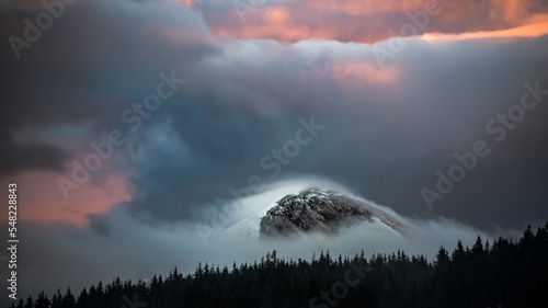 Dramatic Stormy Clouds over the Snowy Mountains of Hoverla snow covered peak in Ukraine. Dramatic light nature forest silhouette background. Hoverla is the higest Ukrainiam mountain. Famous symbol photo