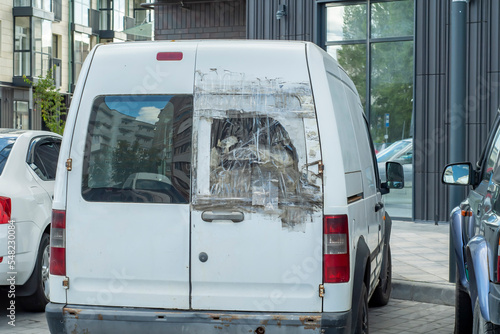 A van with a broken rear window sealed with transparent adhesive tape.