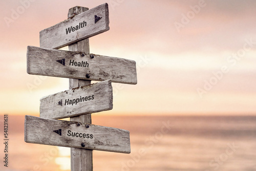 wealth health happiness success text written on wooden signpost outdoors at the beach during sunset