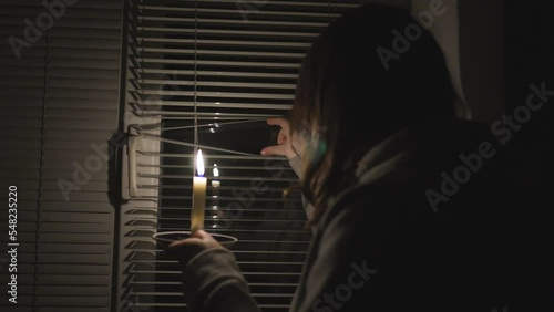Blackout. A girl in a dark room near the window holds a burning candle in her hands
