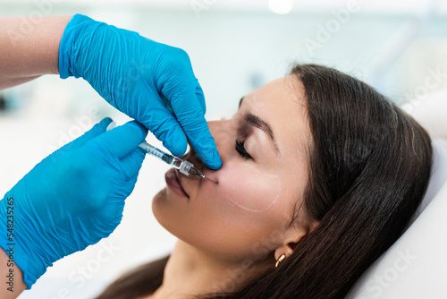 Beautician is contouring the woman's cheekbones with hyaluronic acid filler. Hyaluronic acid filler is injected by needle or cannula. Face contouring concept. photo