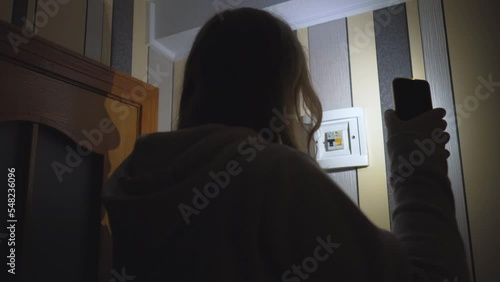Blackout. A girl with a smartphone in her hands checks the electrical panel in the room