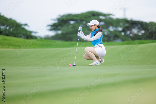 Asian woman golfer sit check line for putting golf ball on green grass,