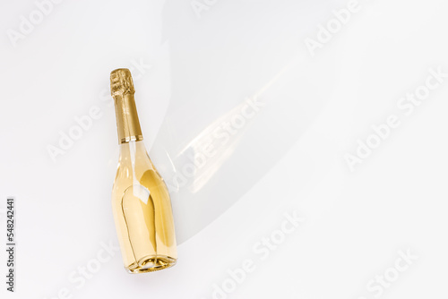 Top view white sparkling wine bottle with sunshine long shadow and flare on light white background. Minimal aesthetic flat lay, one champagne bottle with golden foil. .Summer alcohol drink
