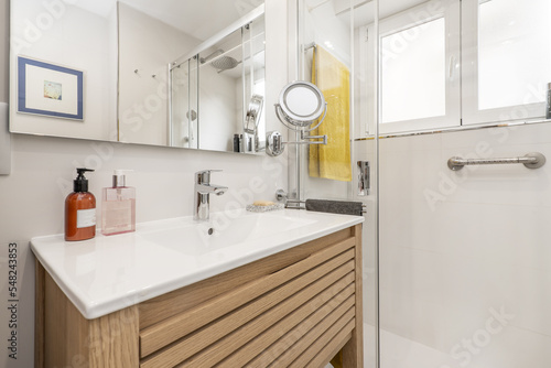 Fototapeta Naklejka Na Ścianę i Meble -  Small bathroom with porcelain sink on oak cabinet, sliding shower stall, frameless mirror and round beauty mirror