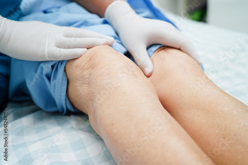 Doctor checking Asian elderly woman patient with scar knee replacement surgery in hospital.