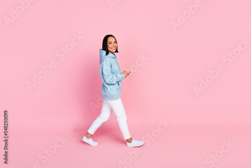 Profile side full length photo of positive lady trendy sportswear walking empty space use modern device isolated on pink color background © deagreez