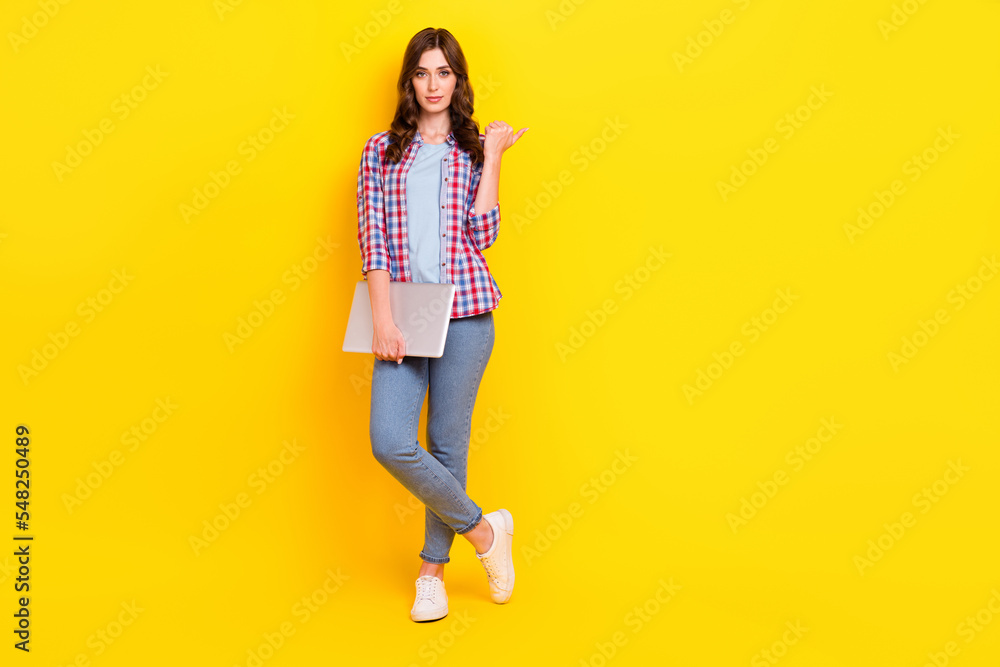 Full length photo of attractive young business lady hold netbook finger point new it company advert empty space isolated on yellow color background Full length photo of attractive young business lady hold netbook finger point new it company advert empty space isolated on yellow color background