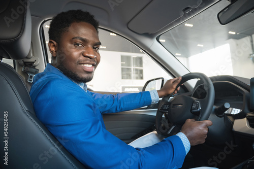 African American man driver enjoys making purchase in automobile salon and prepares to drive. Black happy male customer with excited expression smiles at camera