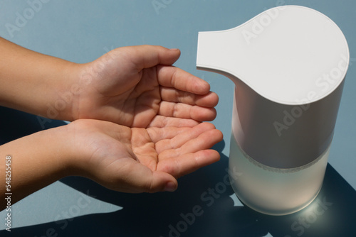 Kids hands near white soap dispenser blue background