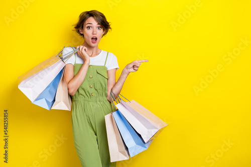 Photo of impressed shocked shopaholic girl hold much package with clothes gifts big sale finger point mockup isolated on yellow color background