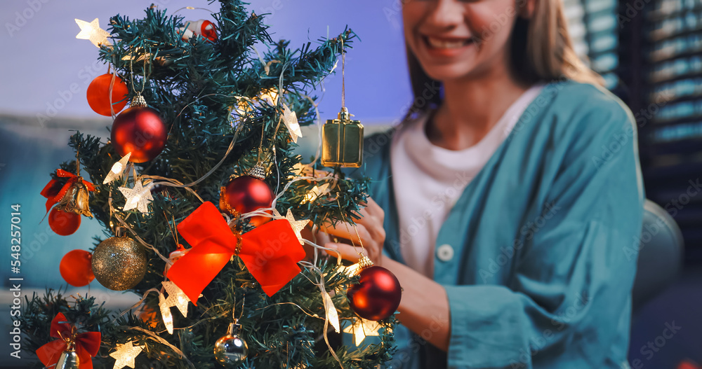 A beautiful woman is decorating a pine tree for a Christmas party at home.