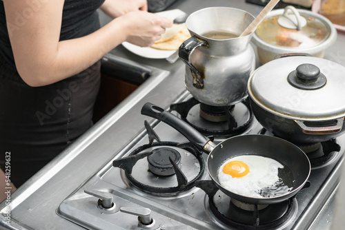 detailed view of a colombian kitchen with a woman preparing a typical breakfast. egg frying in a small frying pan on a gas stove.