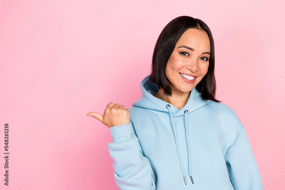 Photo of cute cheerful girl dressed blue sweatshirt smiling pointing thumb empty space isolated pink color background Photo of cute cheerful girl dressed blue sweatshirt smiling pointing thumb empty space isolated pink color background