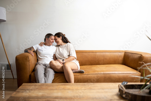 Adult lesbian couple sits on couch at home and smiles