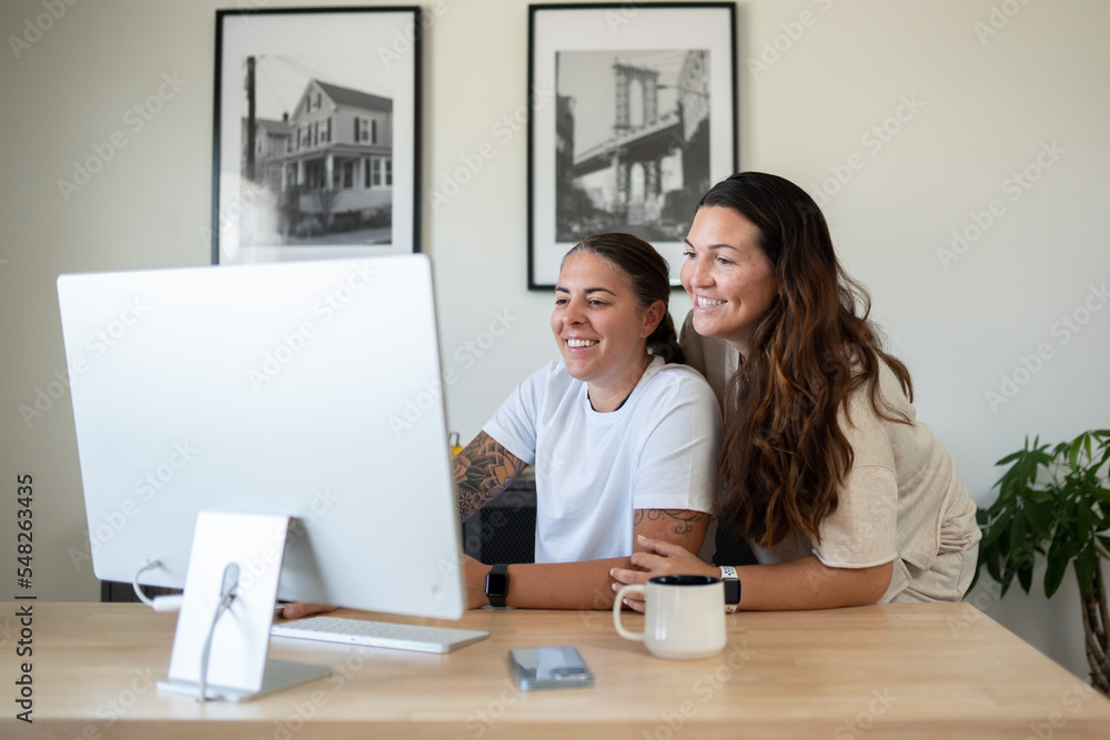 Adult lesbian couple use desktop computer in home office Adult lesbian couple use desktop computer in home office