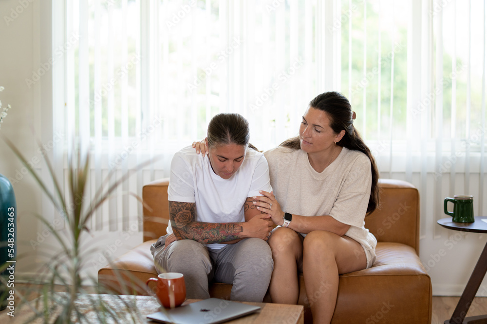 Adult lesbian couple comforting each other on couch at home Adult lesbian couple comforting each other on couch at home