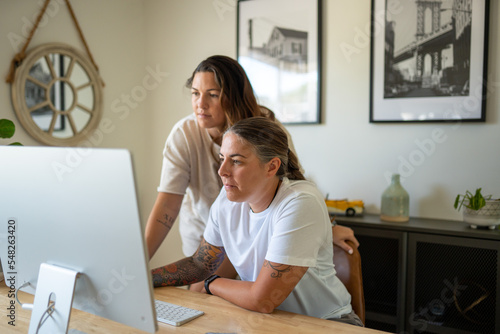 Adult lesbian couple work on desktop computer in home office