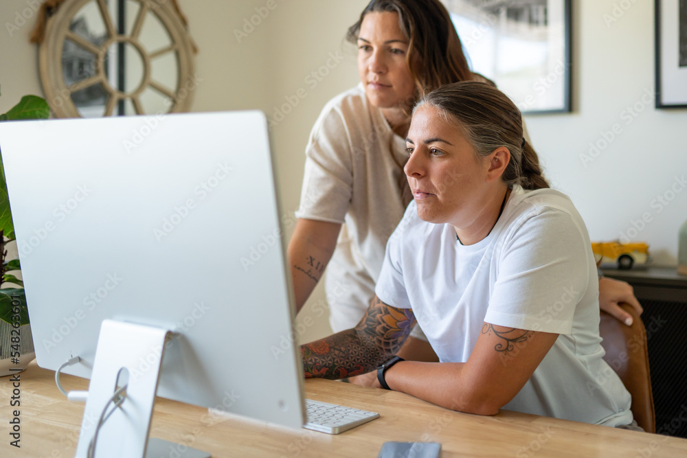 Adult lesbian couple work on desktop computer in home office Adult lesbian couple work on desktop computer in home office
