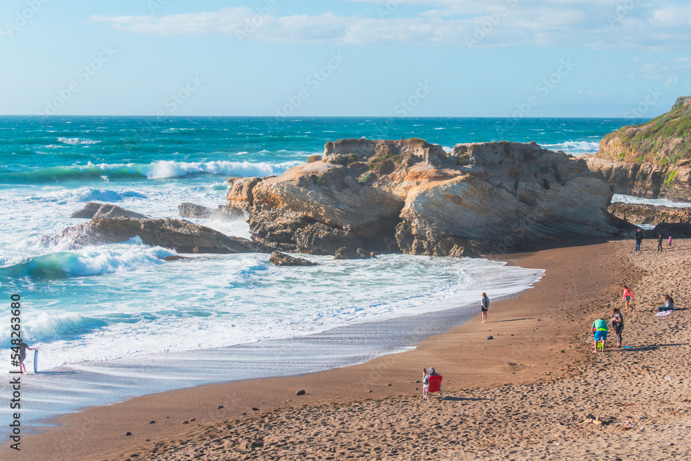 Rocky cliffs, sandy beach, and people enjoying beautiful sunny day. Montana de Oro State park, Los Osos, California Central Coast