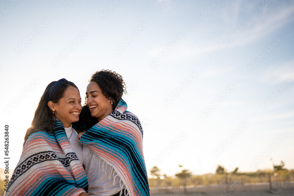 Hispanic lesbian couple uses blanket at beach Hispanic lesbian couple uses blanket at beach