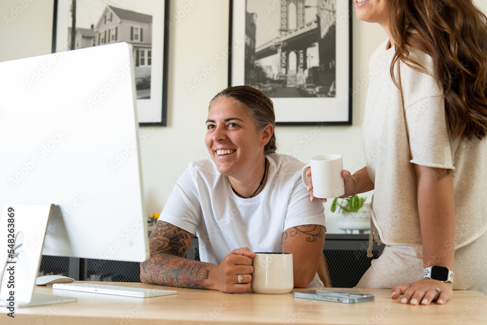 Adult lesbian couple drink coffee while looking at desktop computer Adult lesbian couple drink coffee while looking at desktop computer