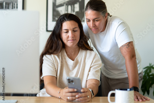 Adult lesbian couple use phone in home office