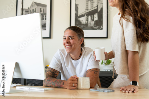 Adult lesbian couple drink coffee while looking at desktop computer