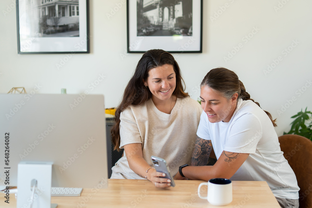 Adult lesbian couple use phone in home office Adult lesbian couple use phone in home office