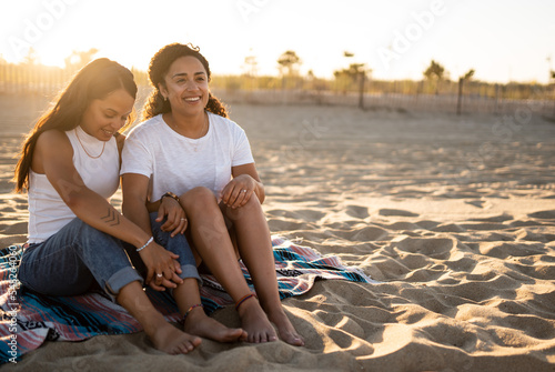 Hispanic lesbian couple sit on a blanket at the beach photo