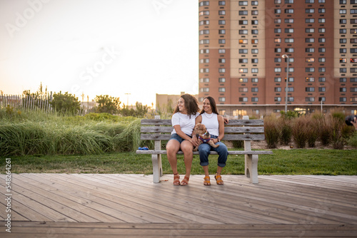 Hispanic lesbian couple sit on a bench with their dog on the boardwalk