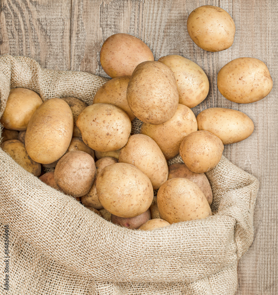 young potatoes scattered from a bag on a wooden table, top view young potatoes scattered from a bag on a wooden table, top view