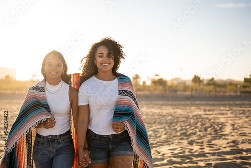 Hispanic lesbian couple walk with blanket at beach photo