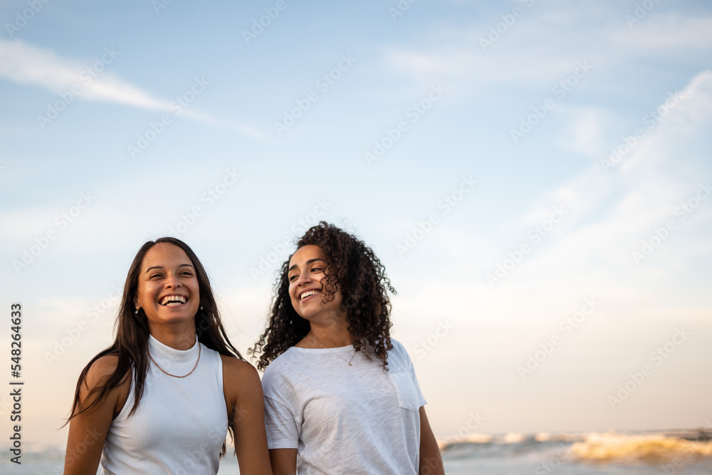 Hispanic lesbian couple walk at the beach holding hands Hispanic lesbian couple walk at the beach holding hands