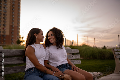 Hispanic lesbian couple sit on a bench with their dog on the boardwalk