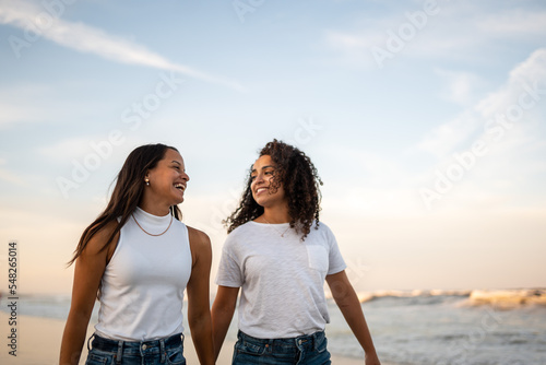 Hispanic lesbian couple walk at the beach holding hands